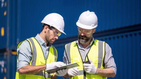 Two inspectors conferring over a clipboard in front of containers